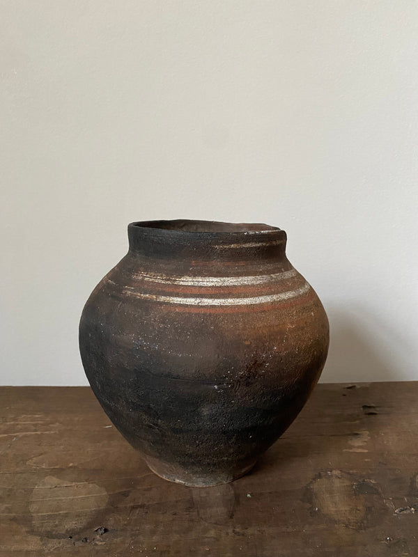 Brown antique clay pot with striped design on a white background