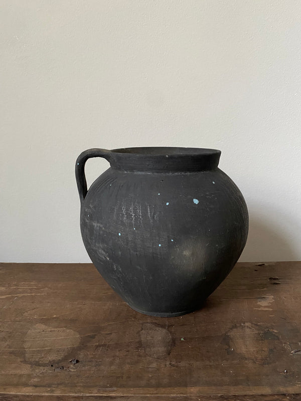 Black antique clay pot on a wooden surface with a white background
