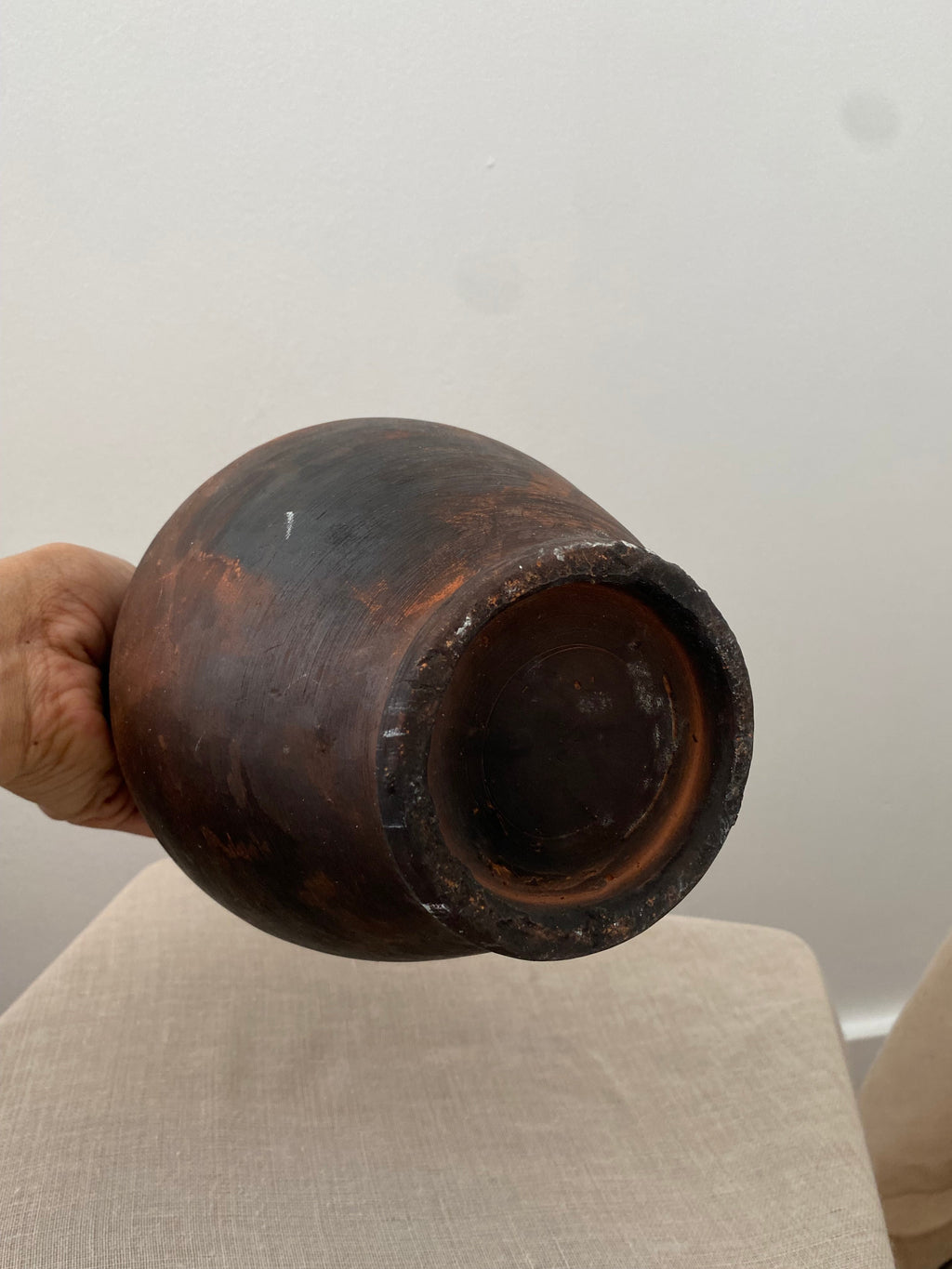 Close up of a Brown antique clay pitcher on a white pedestal against a plain background