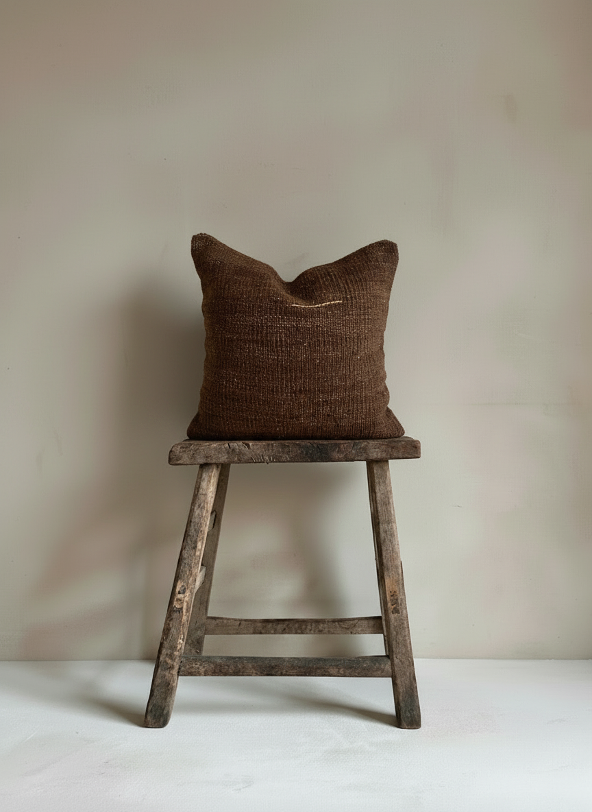 Brown Turkish Kilim pillow cover on a wooden stool against a plain wall