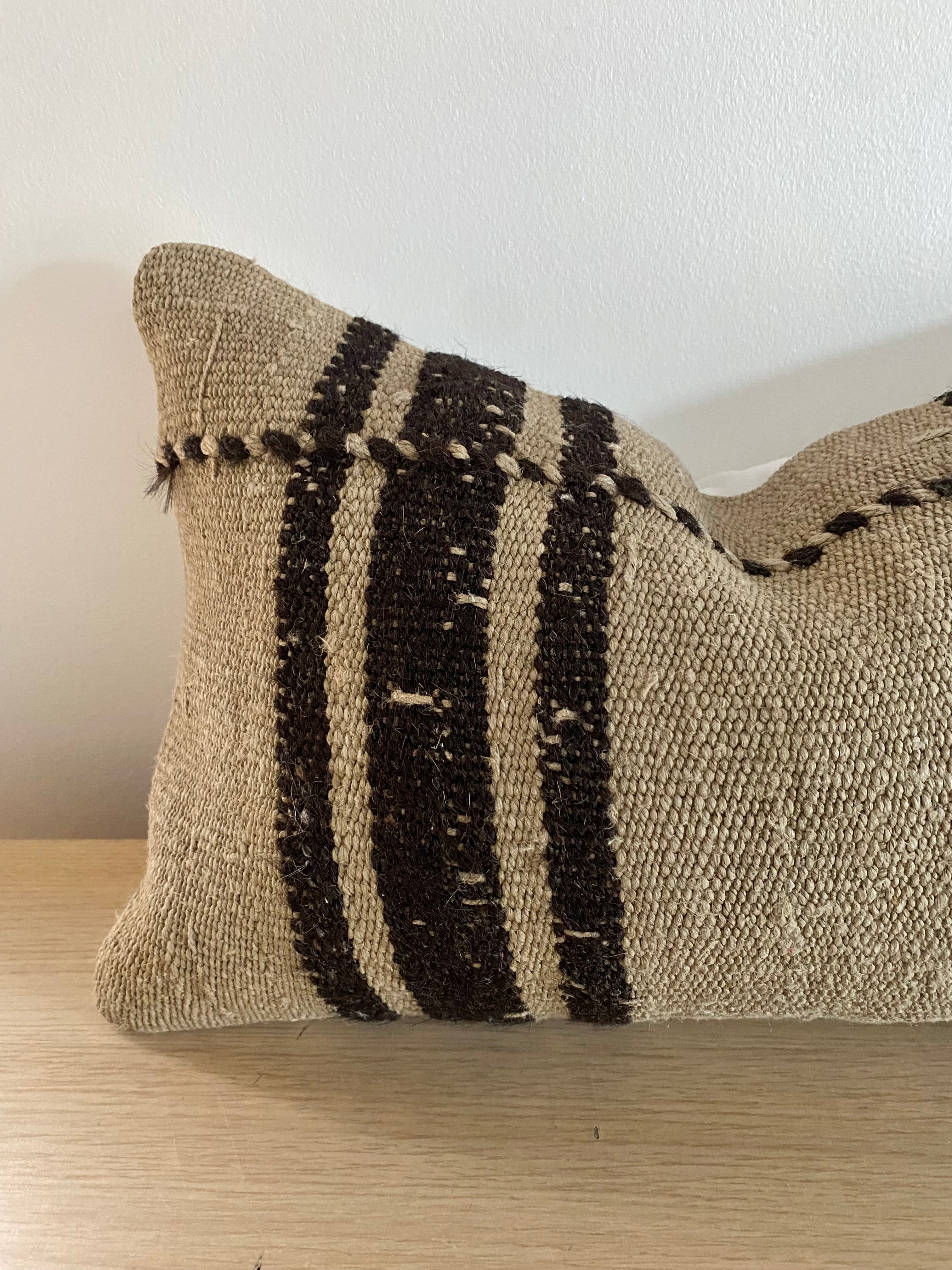 Textured Turkish Kilim pillow cover with black stripes on a wooden surface