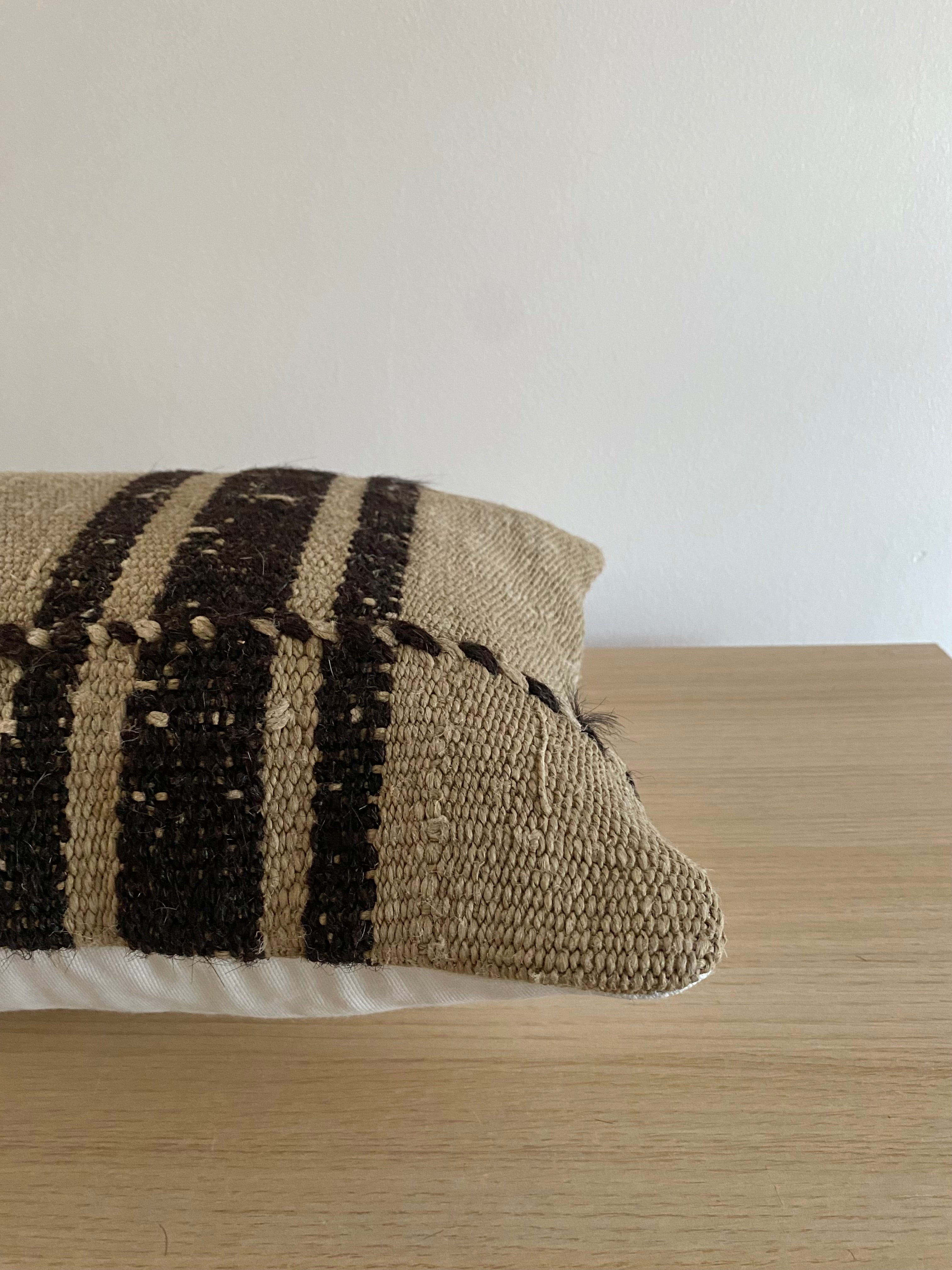 Textured Turkish Kilim pillow cover with black stripes on a wooden surface