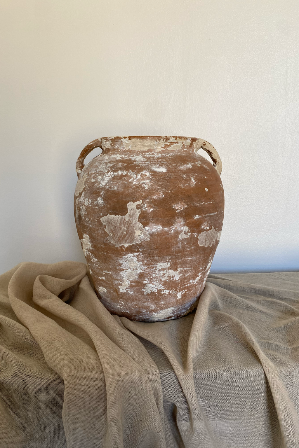 Whitewashed antique terracotta pot with rustic patina, styled on neutral linen perfect for earthy home decor or Mediterranean-inspired interiors.