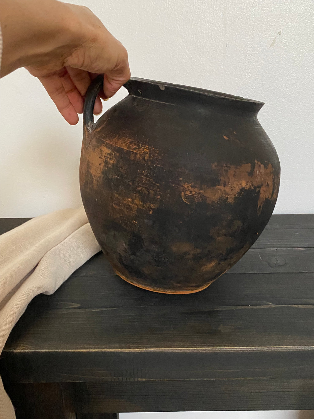 Hand holding an antique terracotta clay pot on a wooden surface