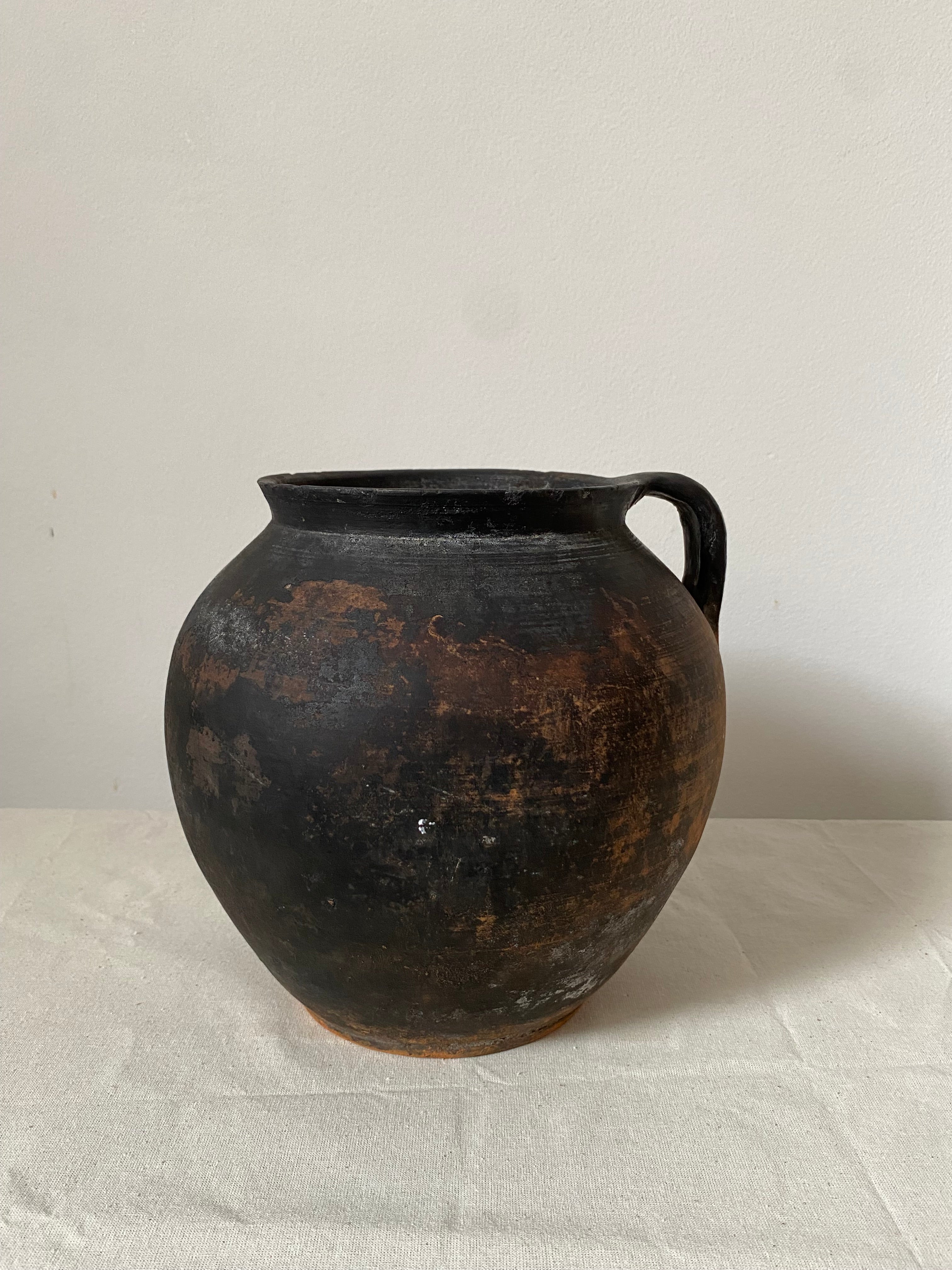 Black antique clay pot with a textured surface on a light gray background