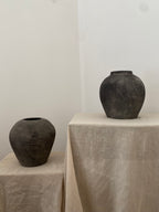 Two black antique terracotta clay pots on beige linen against a white wall
