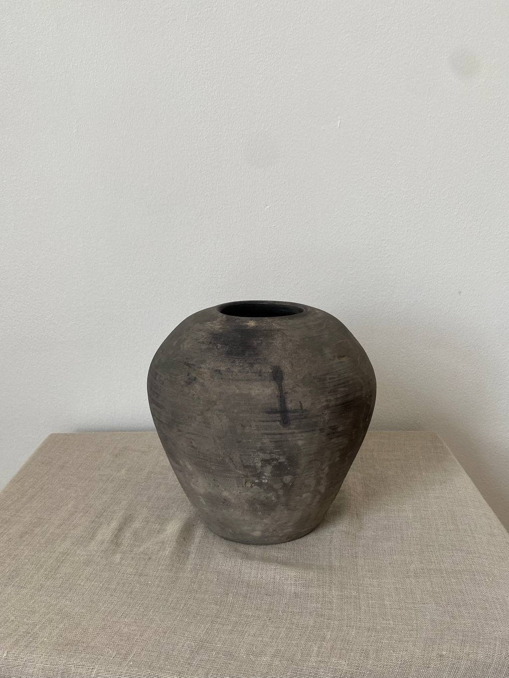Black antique clay vessel on a light linen cloth with a white background