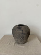 Black antique clay vessel on a light linen cloth with a white background