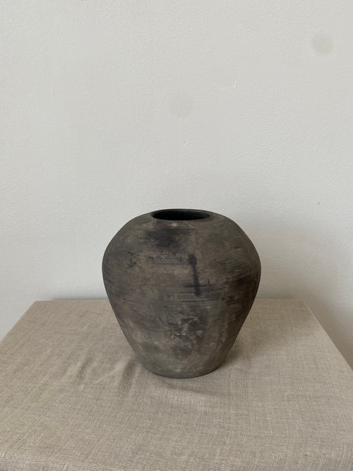 Black antique clay vessel on a light linen cloth with a white background