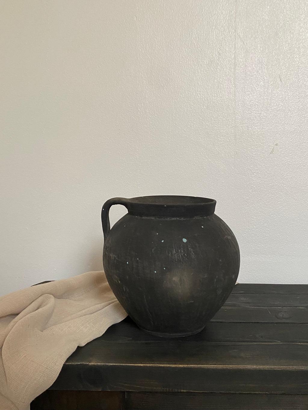 Black antique clay pot against a white wall with a wooden bench