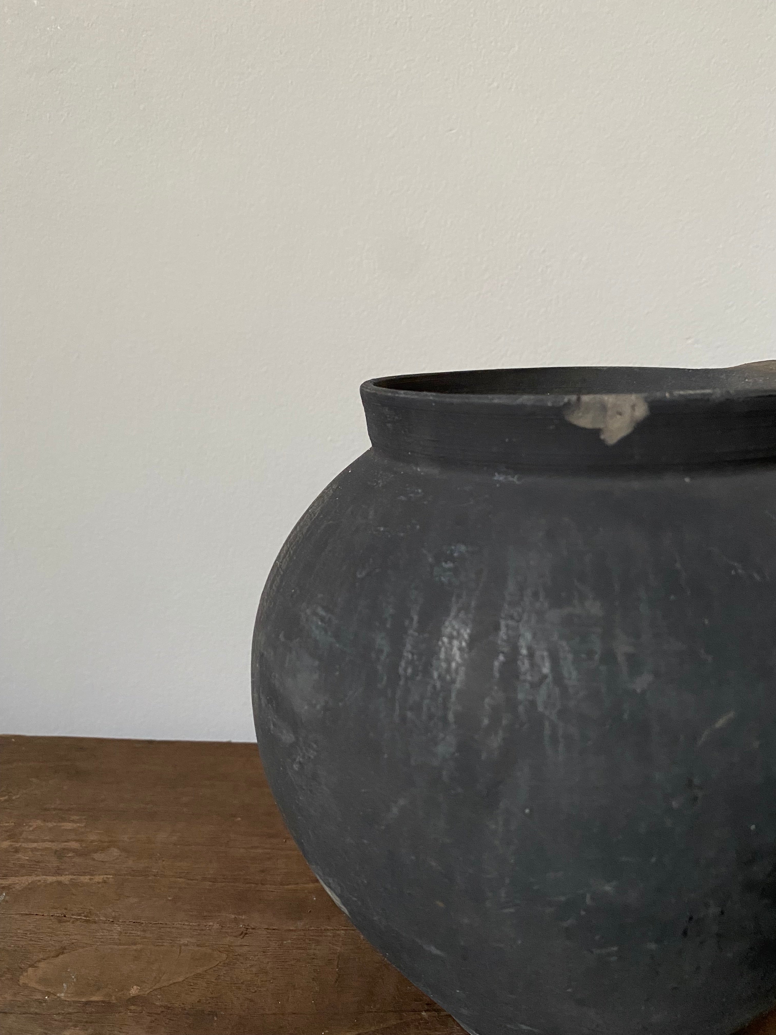Close-up of a black antique terracotta clay pot on a white surface with a wooden background