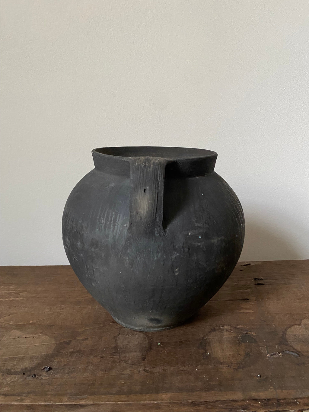 Black terracotta vase on a wooden surface with a white background