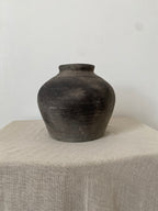 Black grey Q toque clay pot on a light wooden surface with a white background
