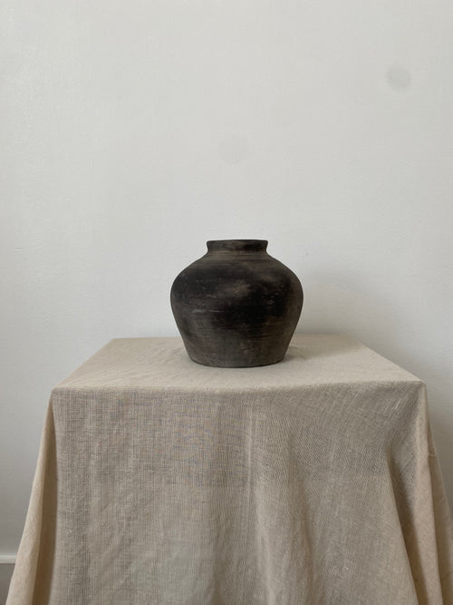 Black grey clay pot on a beige pedestal against a white background