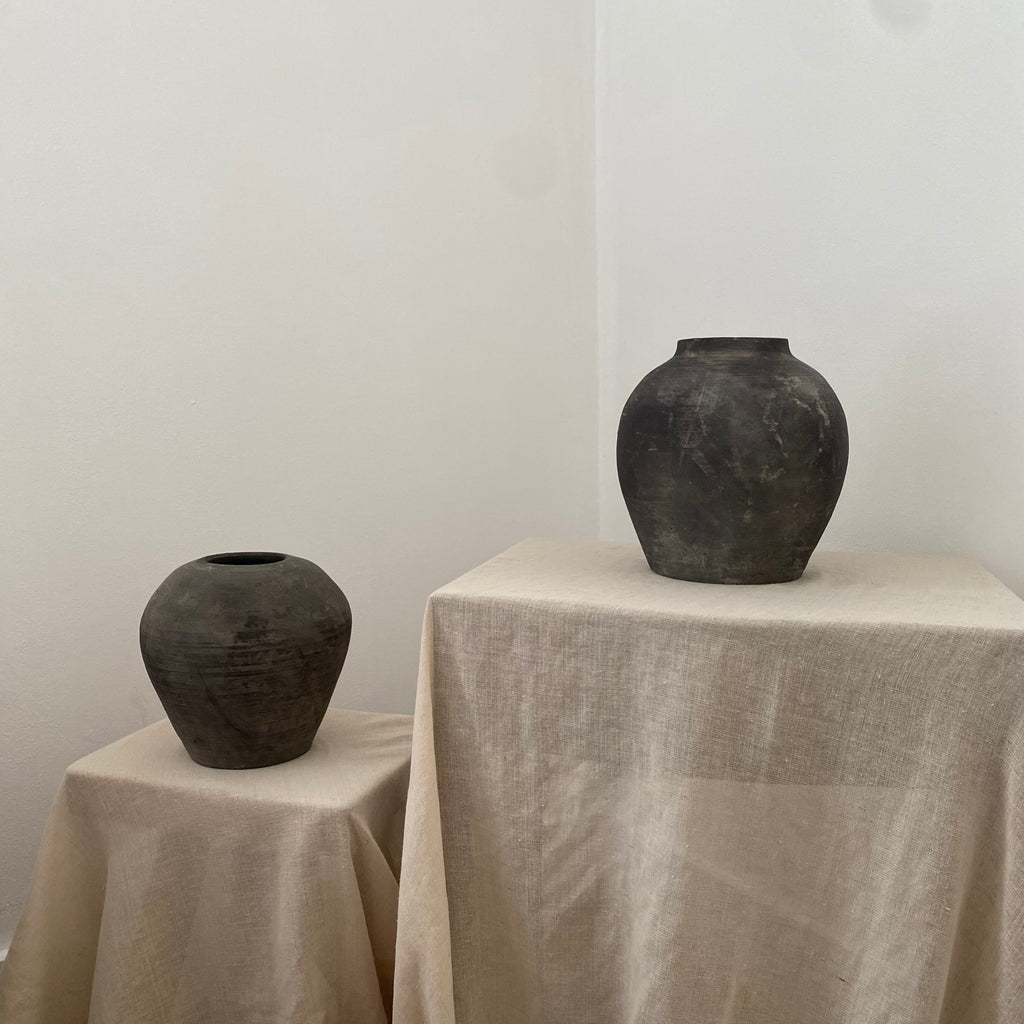 Two black grey clay pots on a beige tablecloth with a plain white background