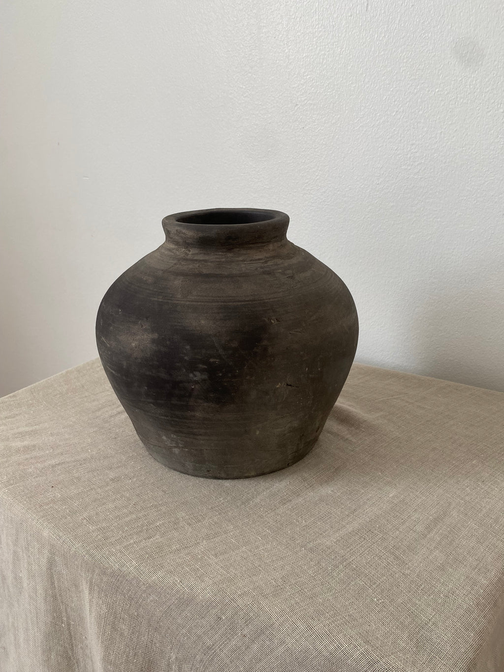 Black grey antique clay pot on a textured linen fabric with a neutral background
