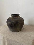 Black grey antique clay pot on a textured linen fabric with a neutral background