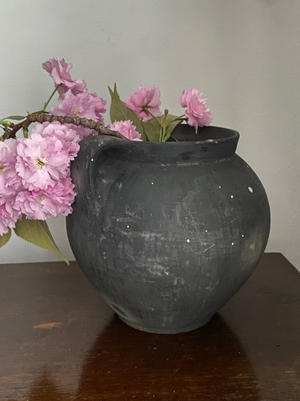 Black antique terracotta clay pot with pink flowers on a white background