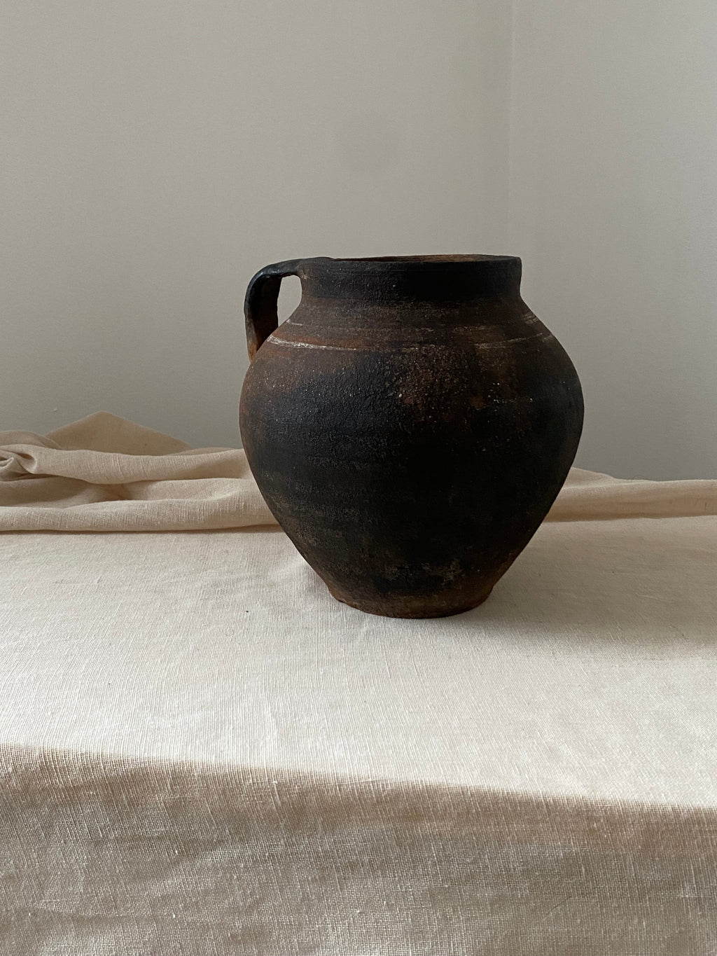 Black antique clay pot on a white surface with a neutral background