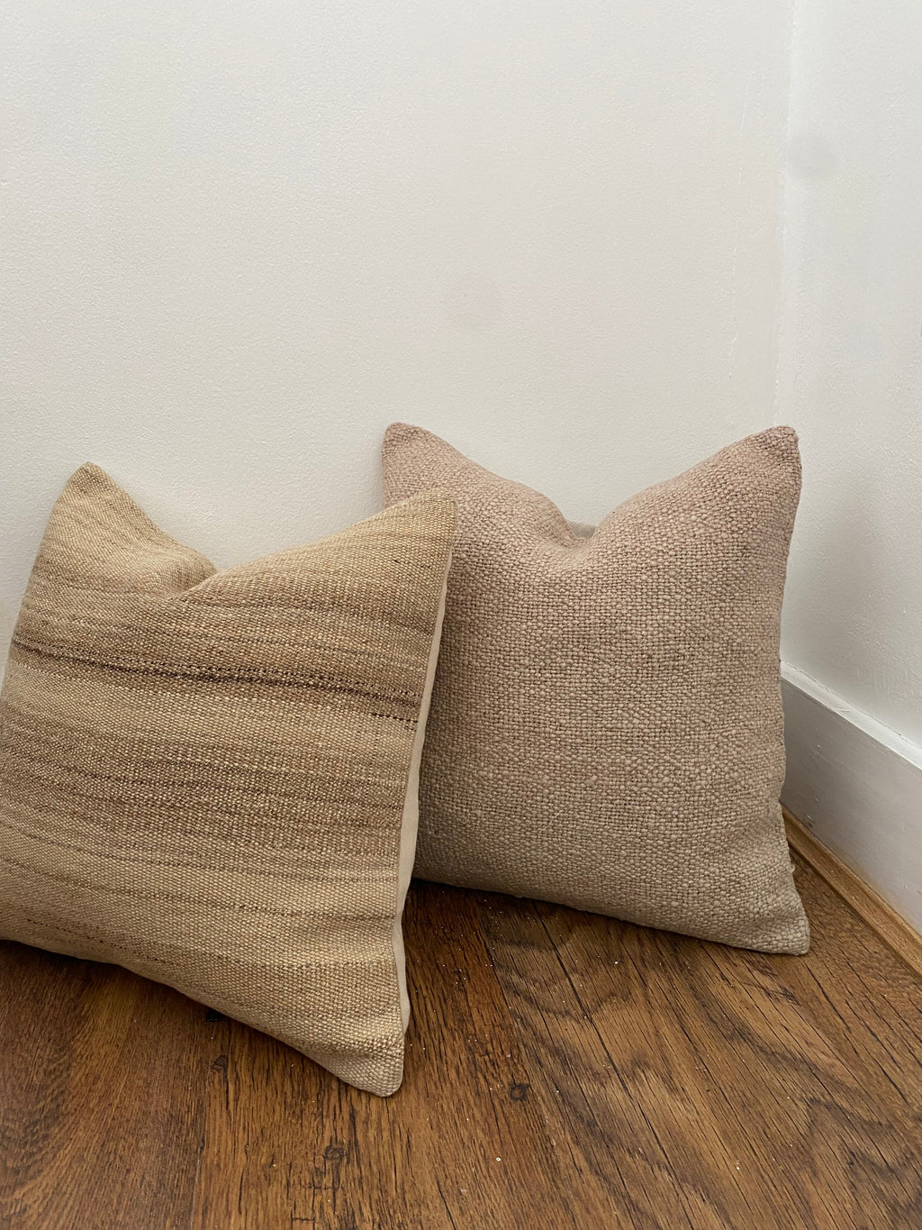 Two beige textured Anatolian pillow covers on a wooden floor against a white wall.