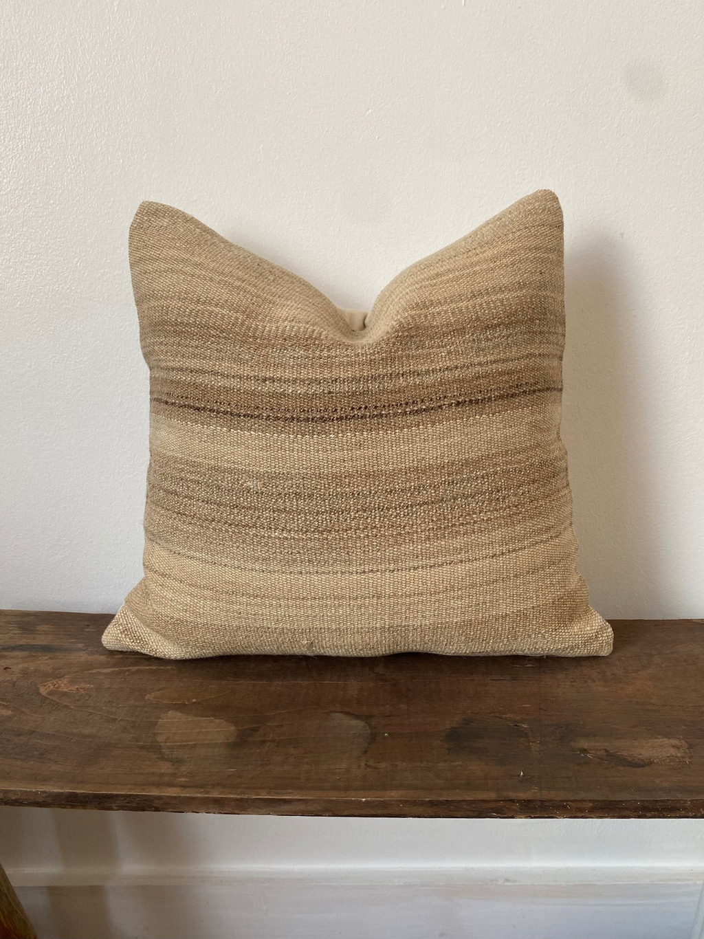 Textured beige Turkish Kilim pillow cover on a wooden surface with a white background