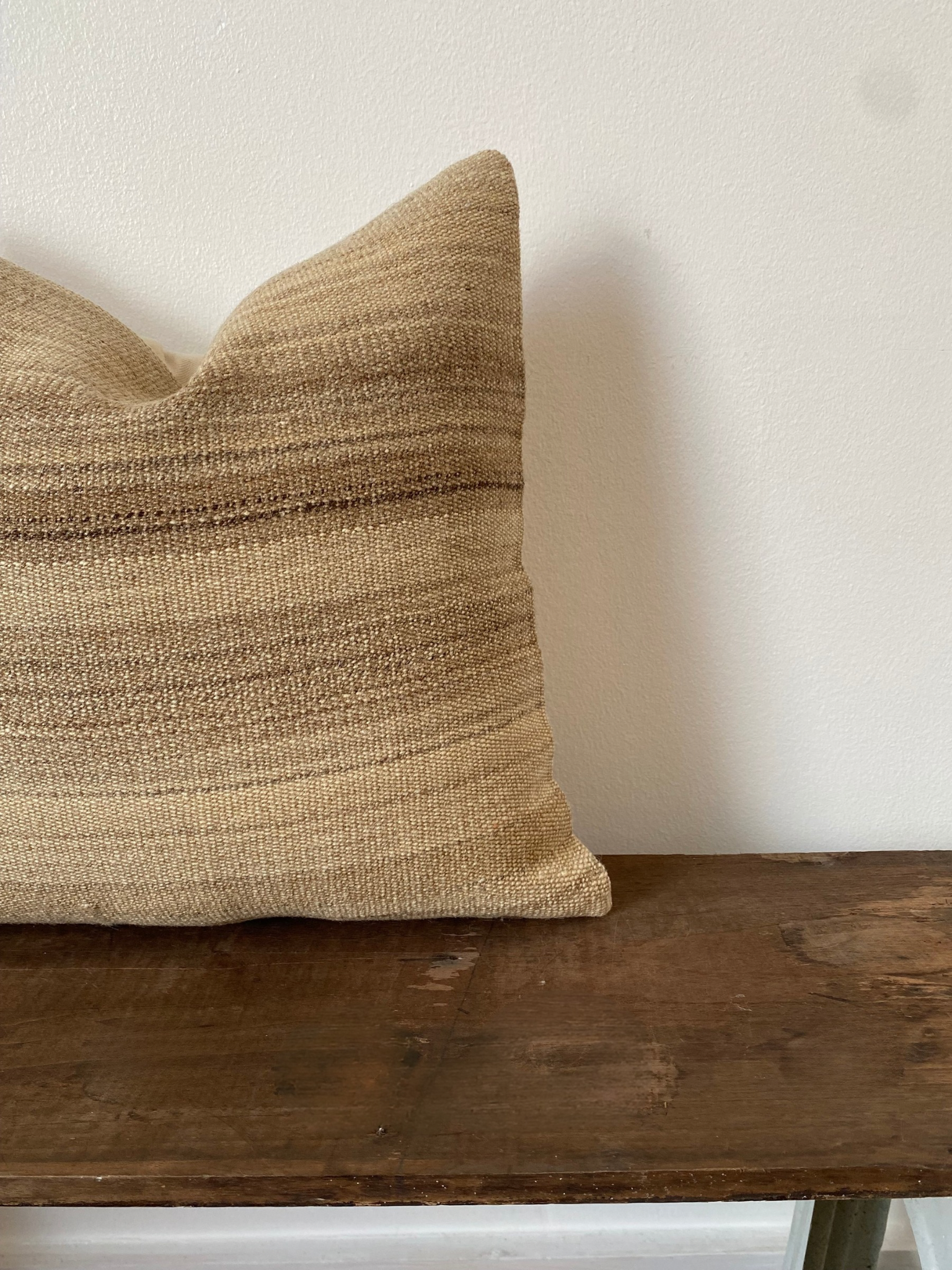 Textured beige Turkish Kilim pillow cover on a wooden bench against a white wall