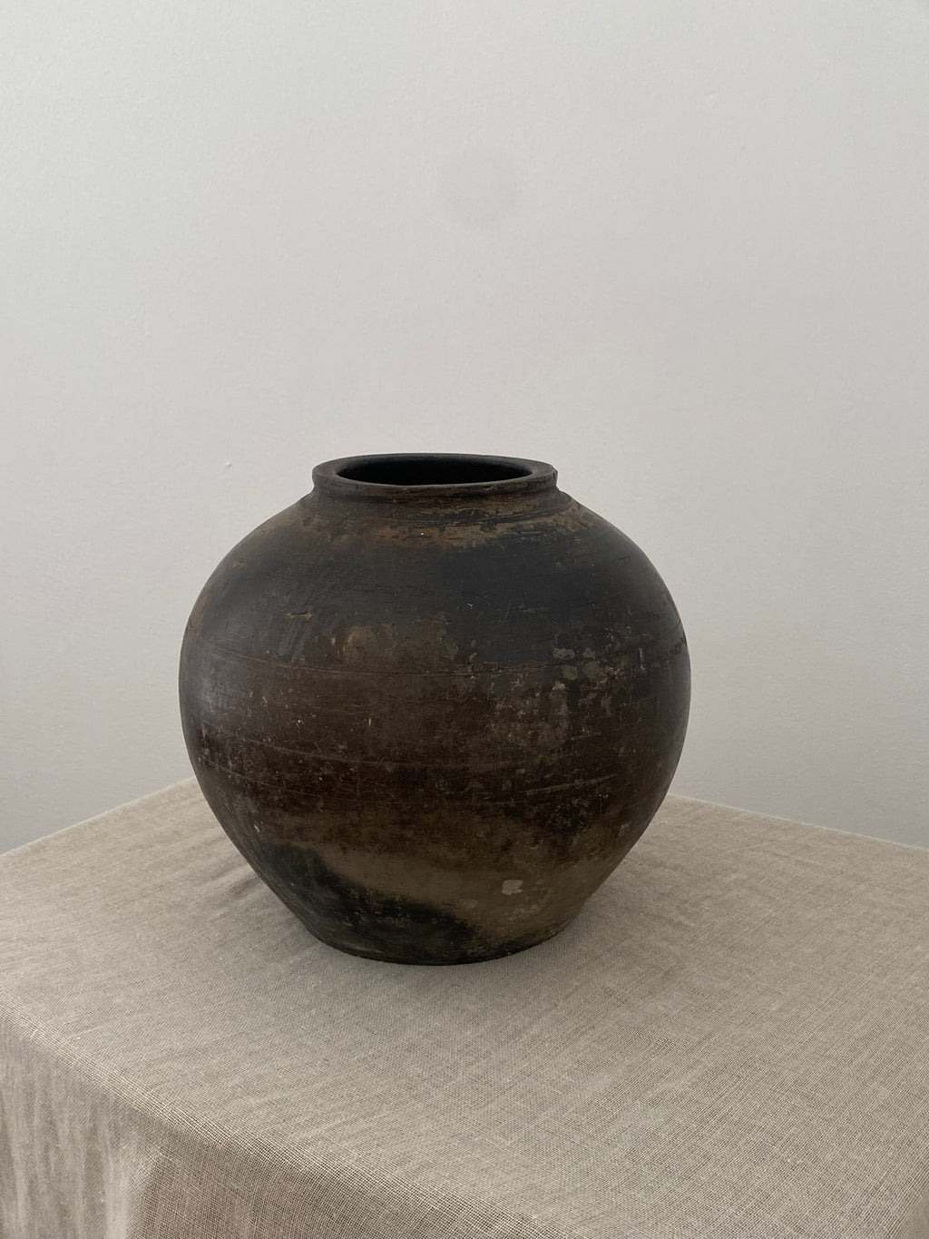 Dark brown terracotta clay pot on a light linen cloth with a white background