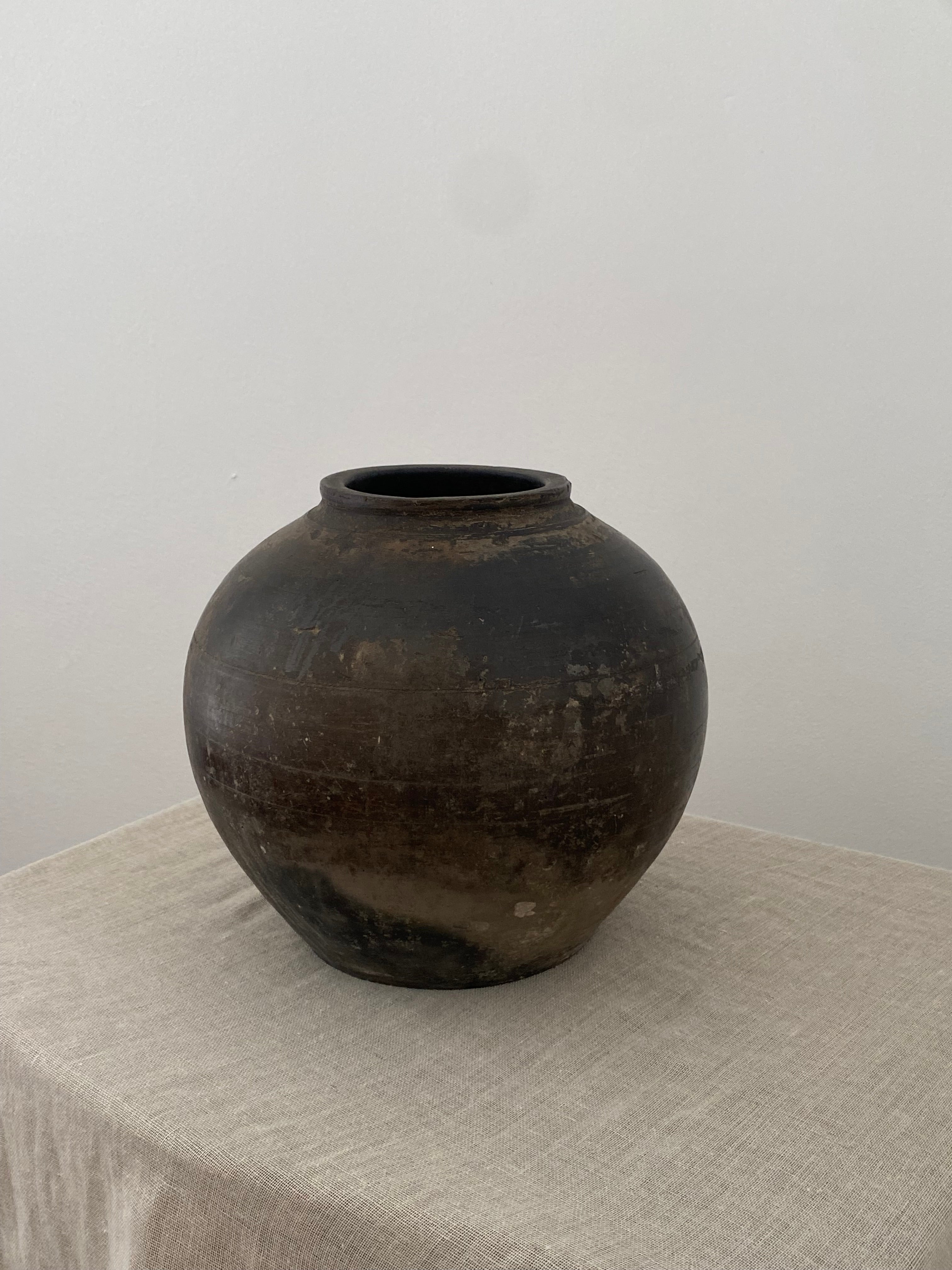 Dark brown terracotta clay pot on a light linen cloth with a white background
