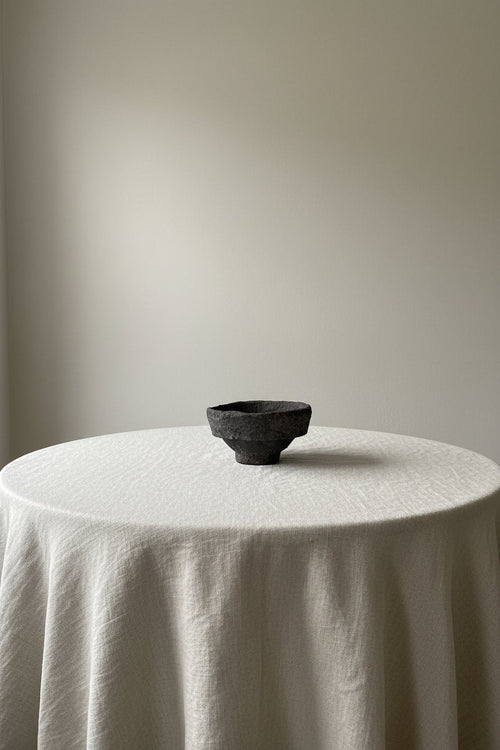 Black papermche bowl on a round table with a plain background