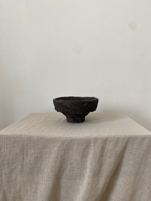 Black papiermache bowl on a beige tablecloth with a plain white background