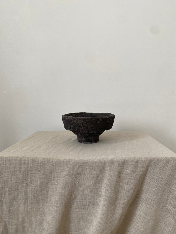 Black papiermache bowl on a beige tablecloth with a plain white background