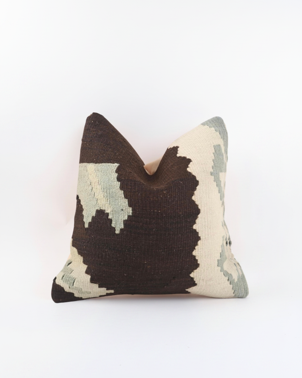 A square brown Turkish Kilim decorative throw pillow cover featuring a textured, woven kilim pattern in dark brown, cream, and sage green, set against a plain white background.