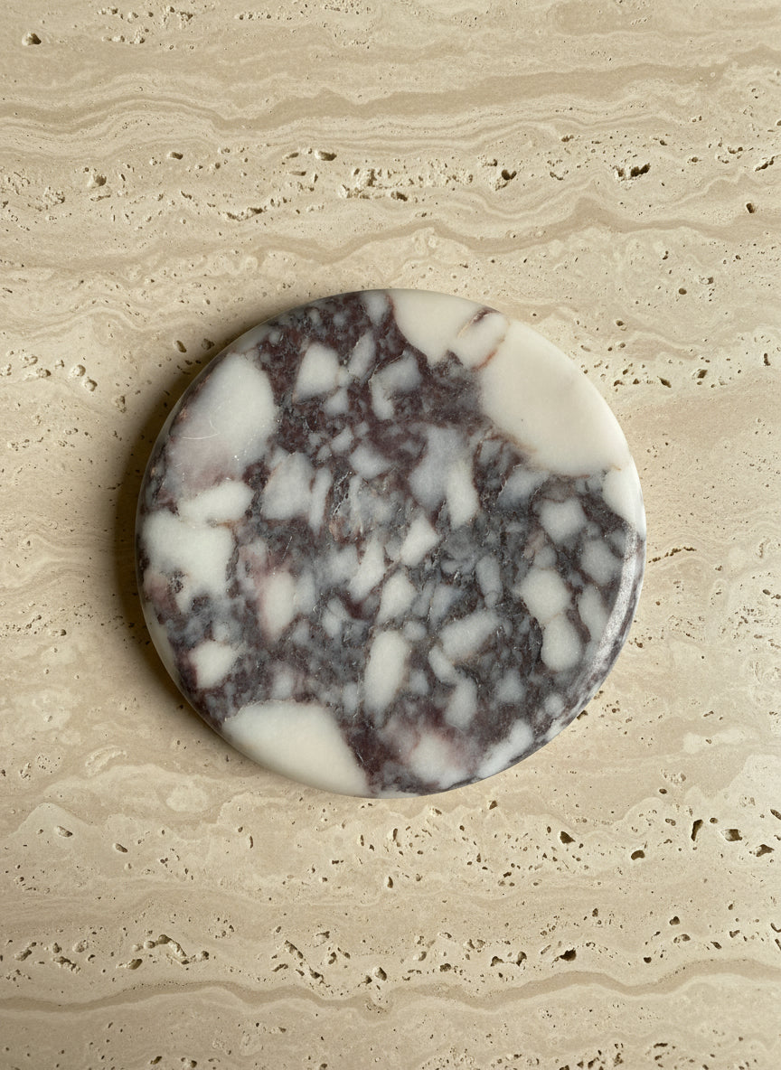 Round Calcutta Marble-patterned coaster on a book titled 'The Art of Home'.