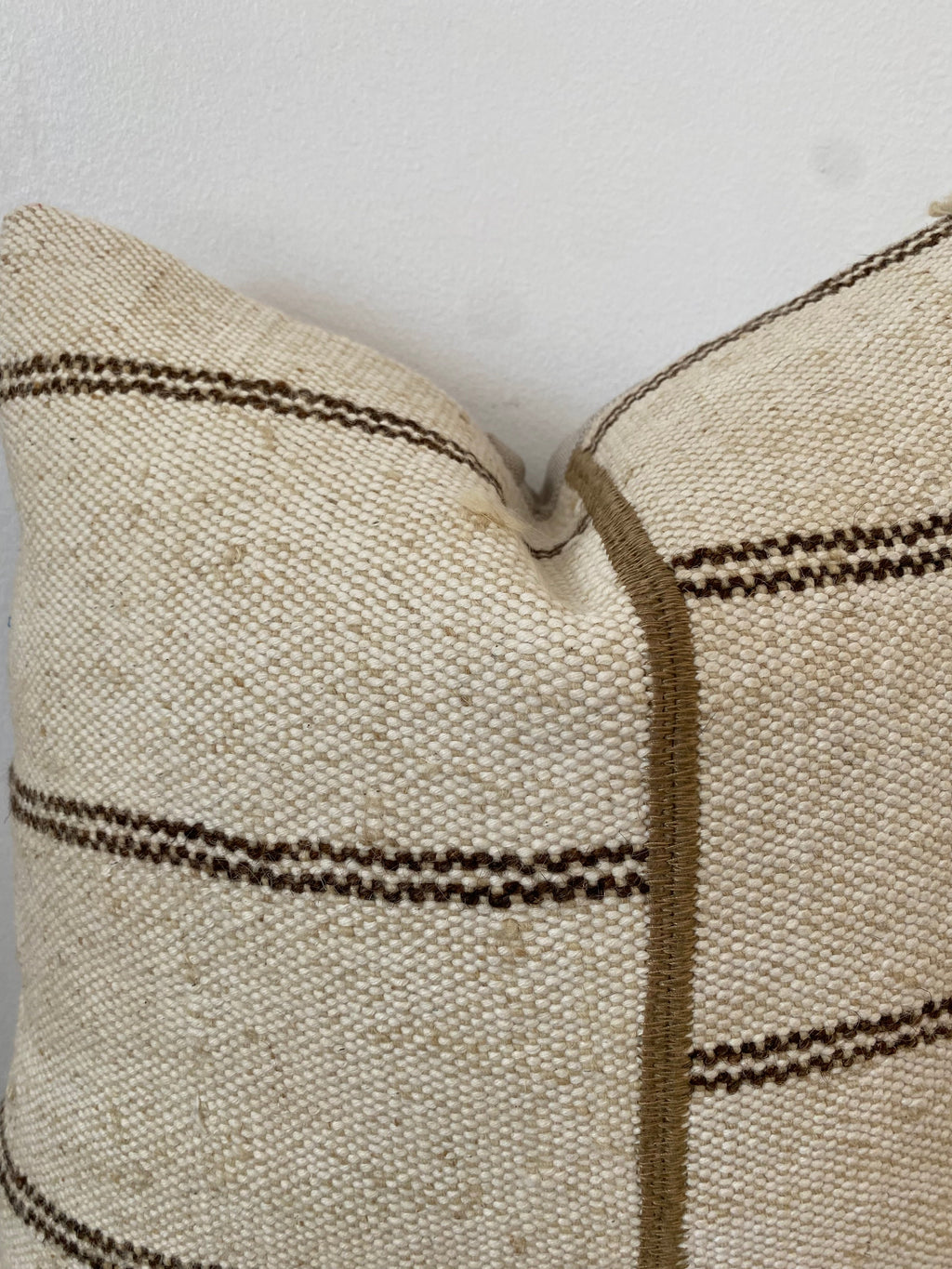 Close-up of a textured cream pillow cover with brown stripes on a light background