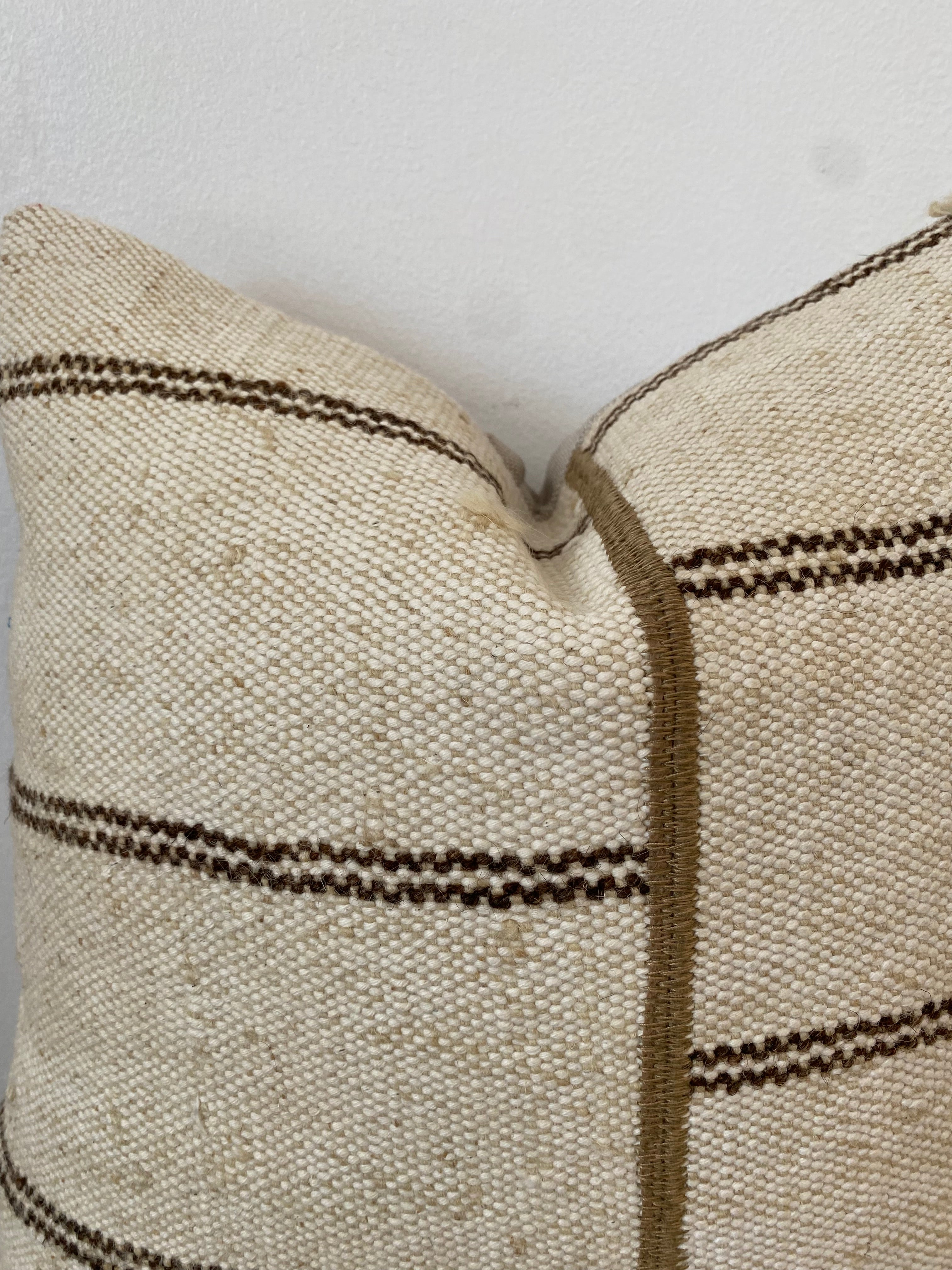 Close-up of a textured cream pillow cover with brown stripes on a light background
