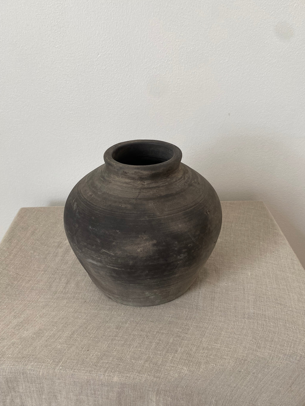 Black grey antique clay pot on a beige linen fabric with a white background