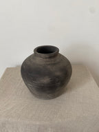 Black grey antique clay pot on a beige linen fabric with a white background