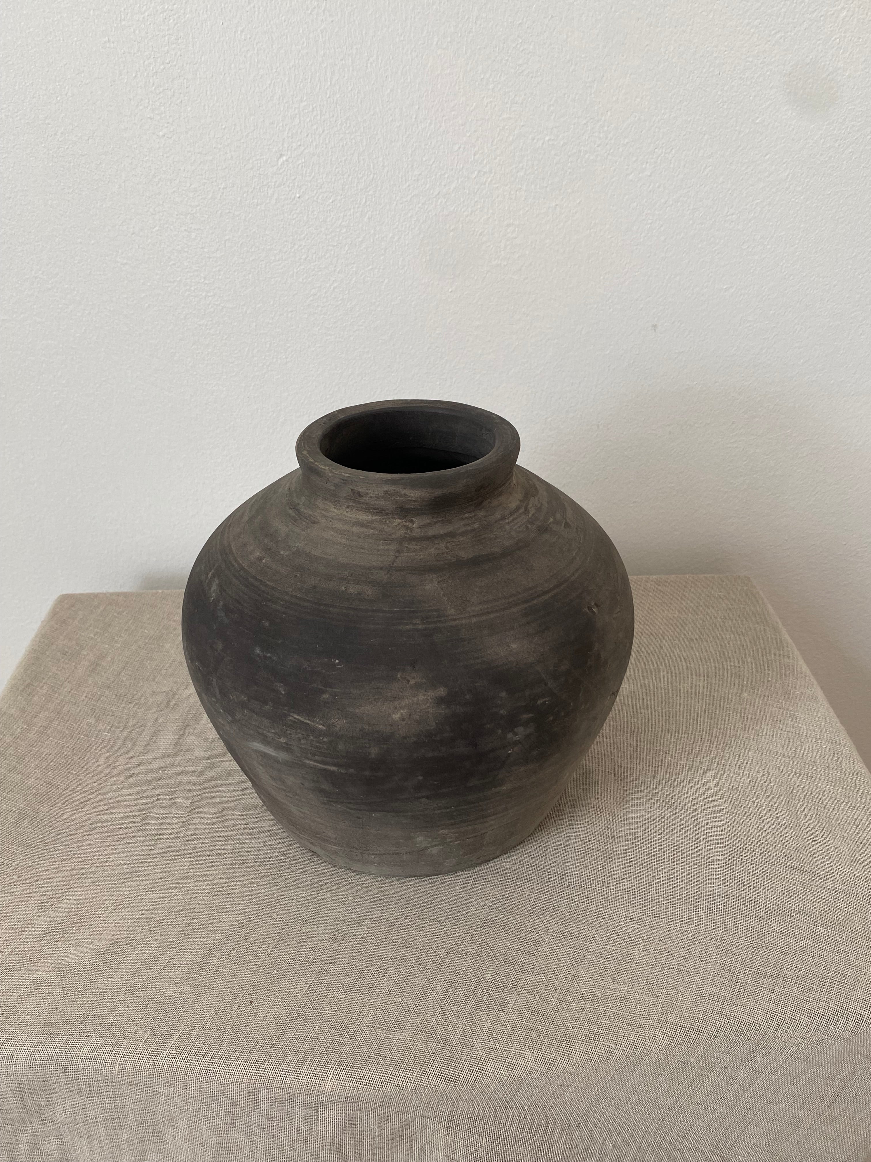 Black grey antique clay pot on a beige linen fabric with a white background