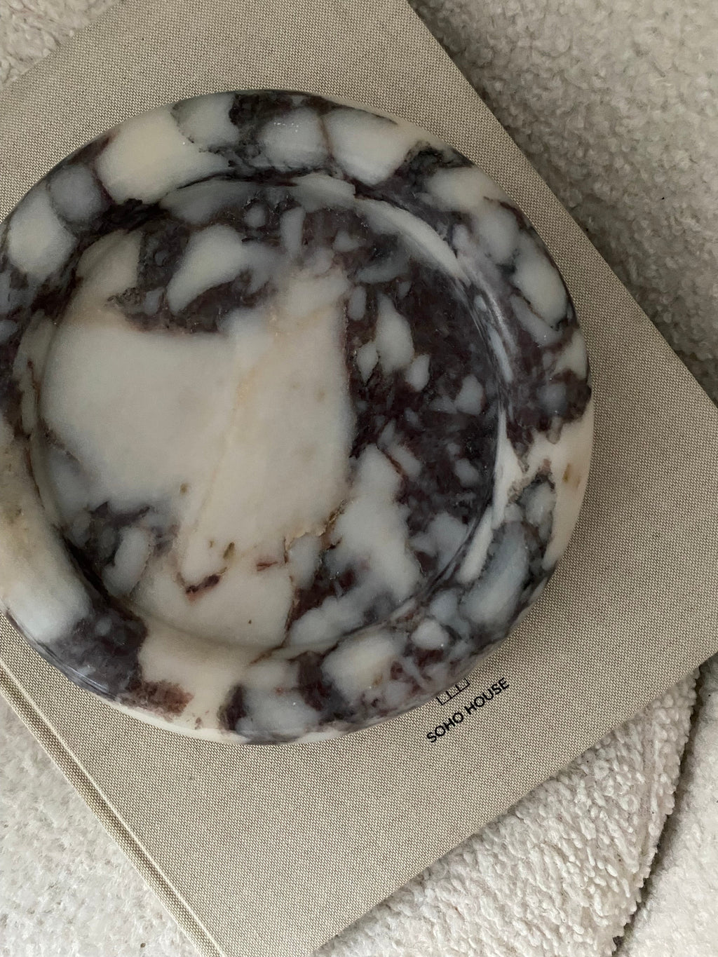 Calacatta Viola Marble round tray on a beige surface with 'on a Soho Home decorative' book.