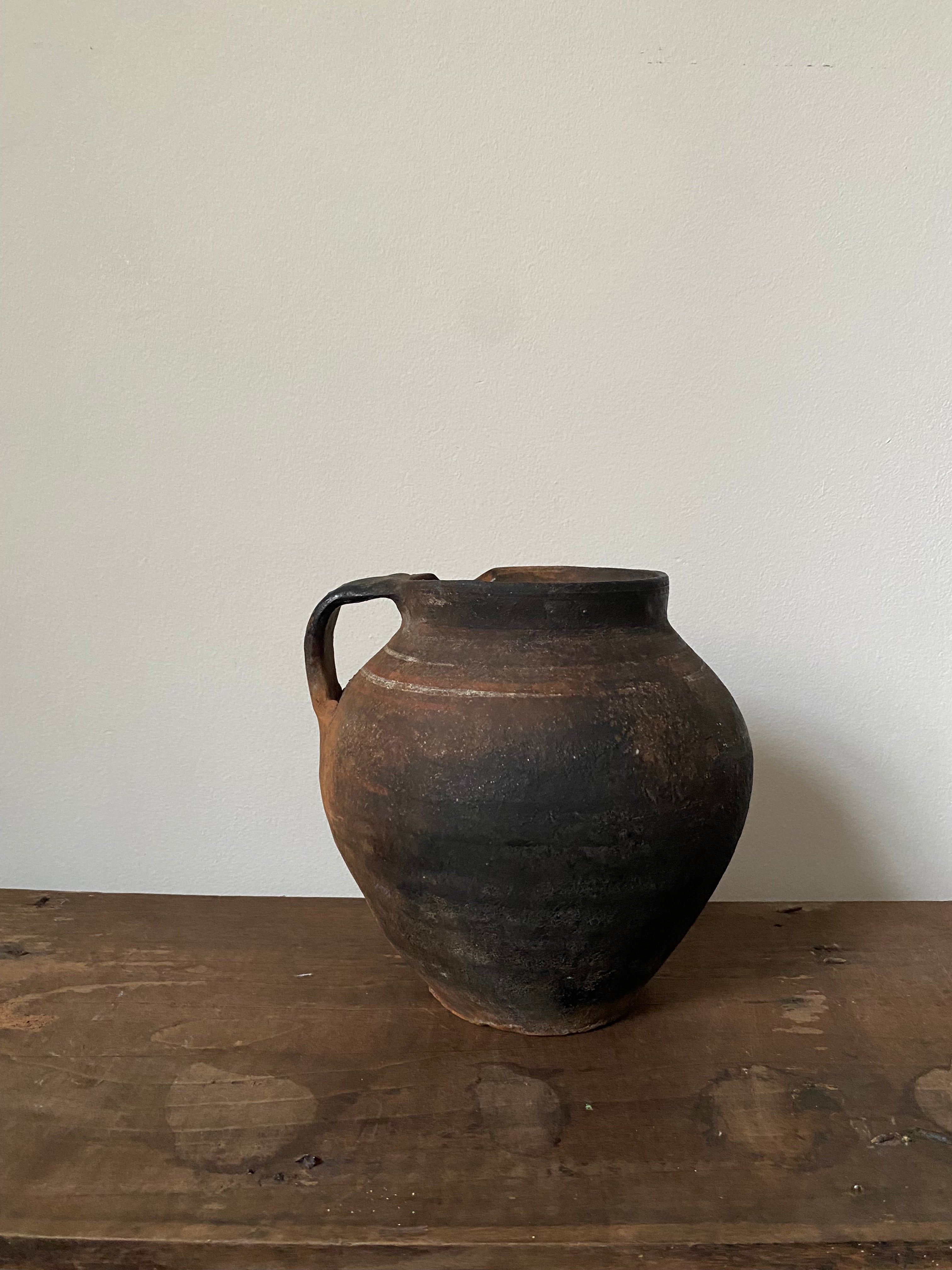 Black Ukrainian weathered antique clay  pot with one handle on wooden surface