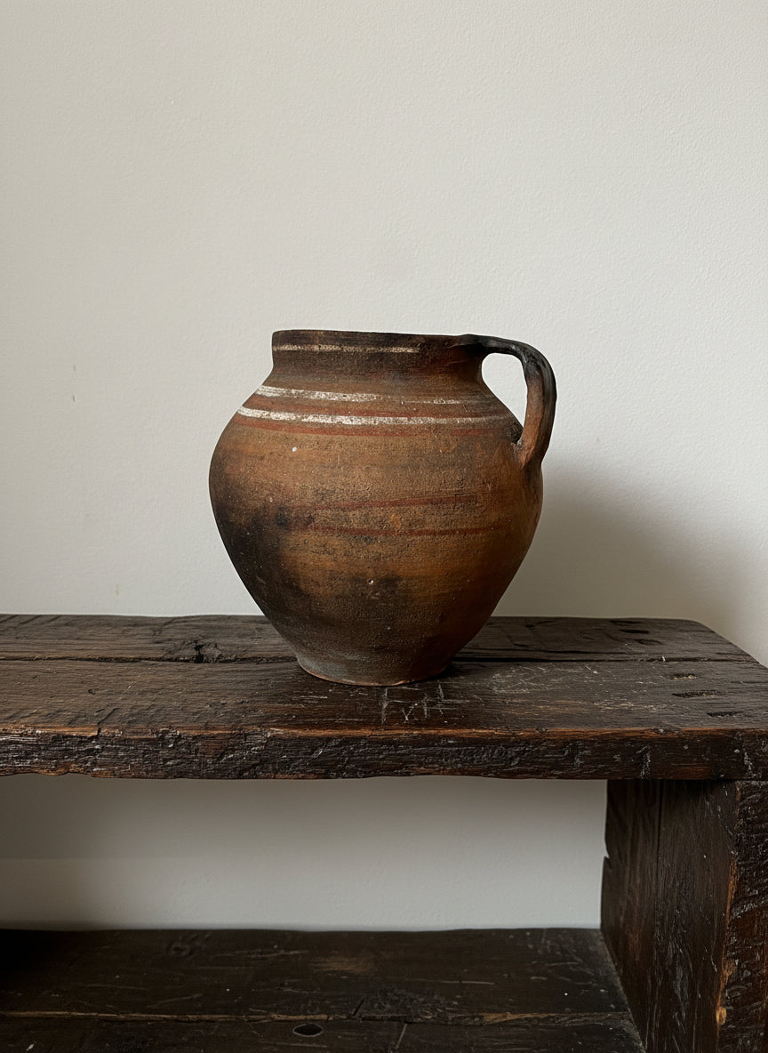 Brown ceramic vase with a handle on a light gray background