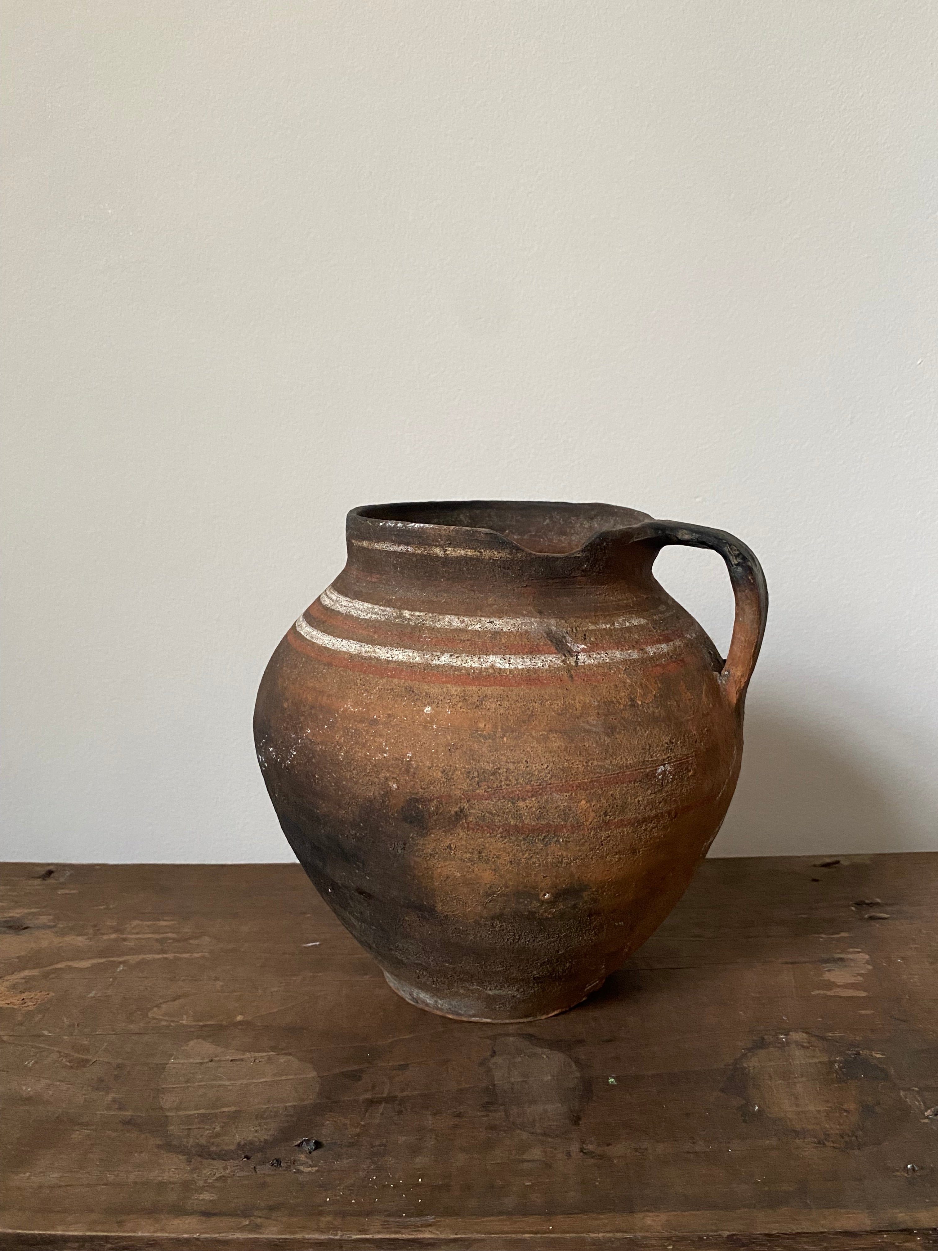 Brown antique clay pot with a handle on a wooden surface