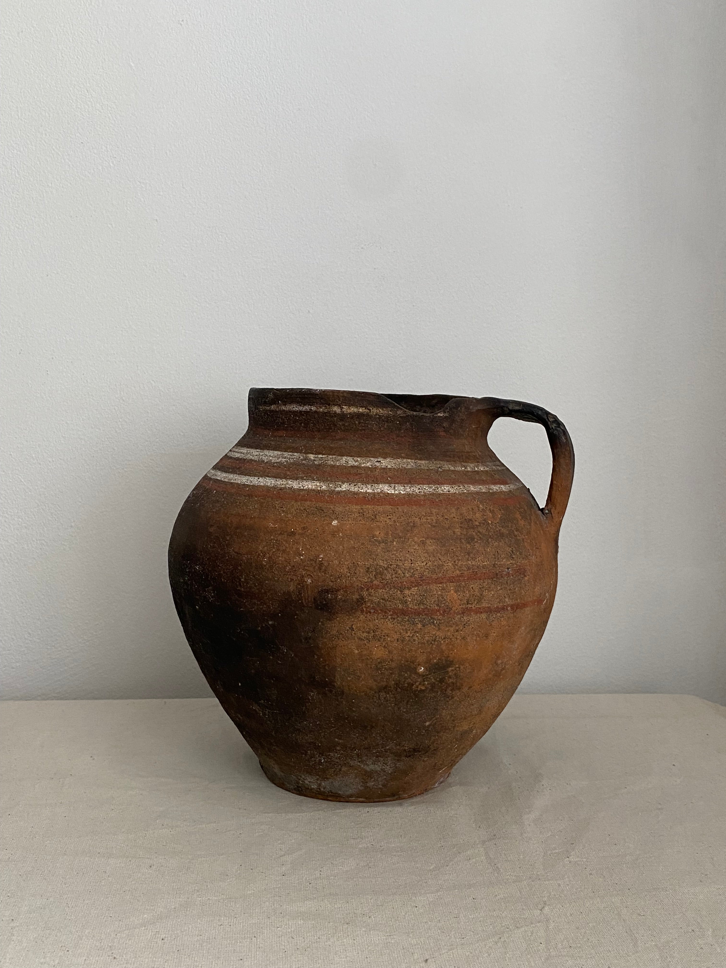 Brown antique clay pot jug with a single featuring two vertical white painted stripes, shown against a plain light gray background.