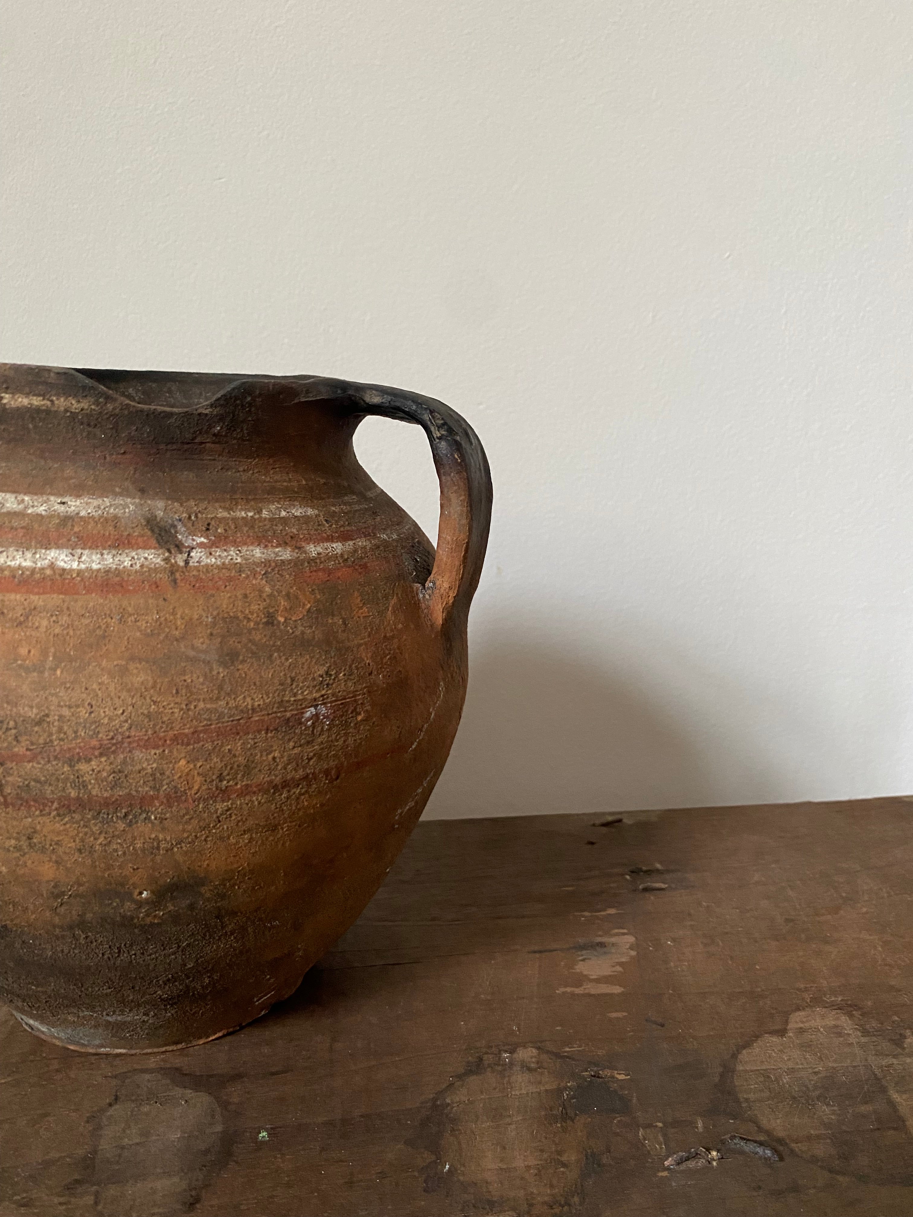 Close-up of a textured brown antique clay pot against a white background on a wooden table