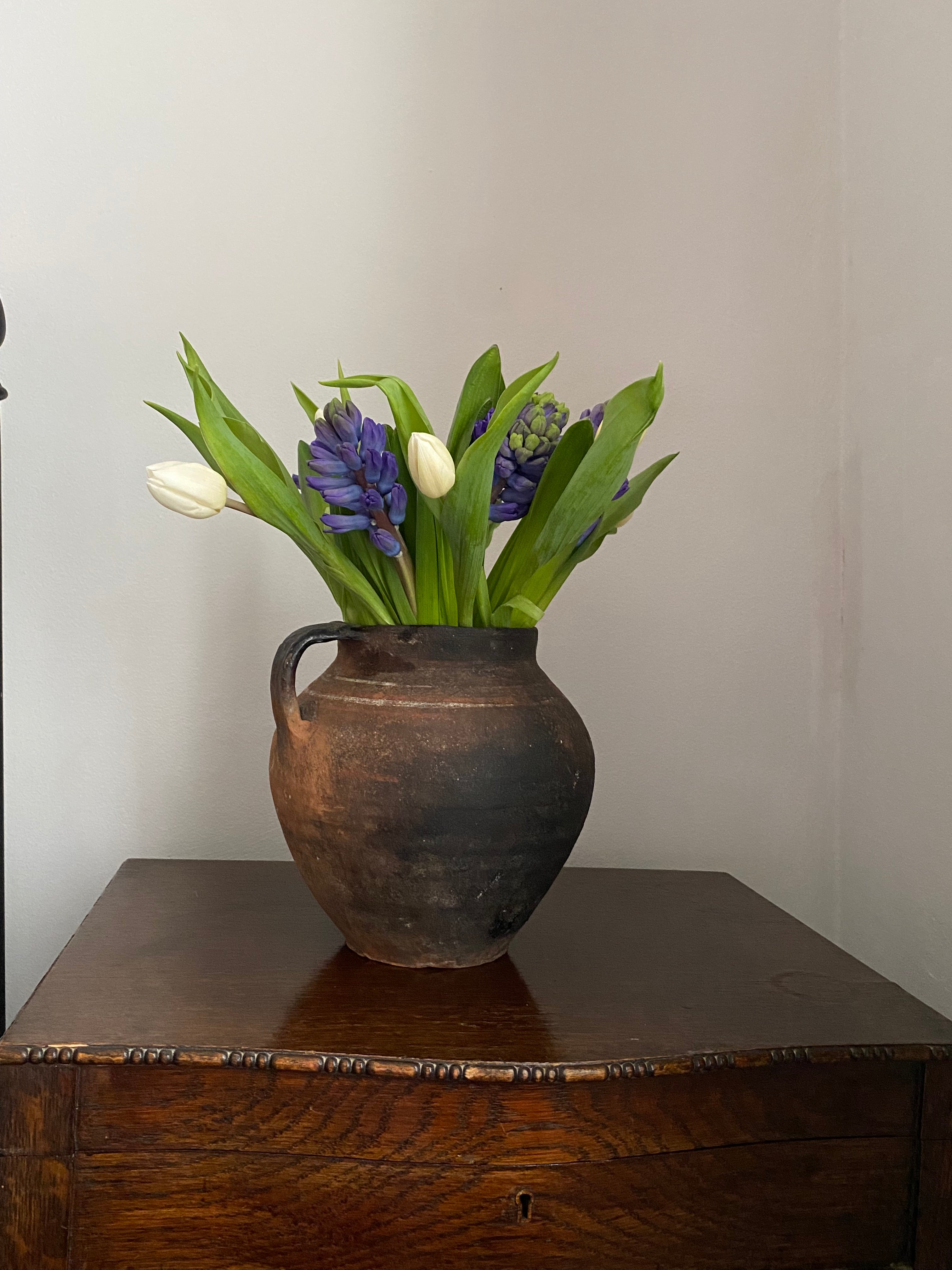 Decorative vintag  vase with flowers against a neutral wallon a good wooden console