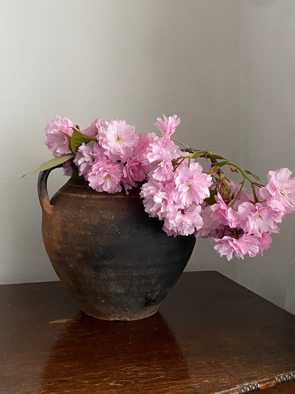 Antique clay pot with pink flowers on a wooden table