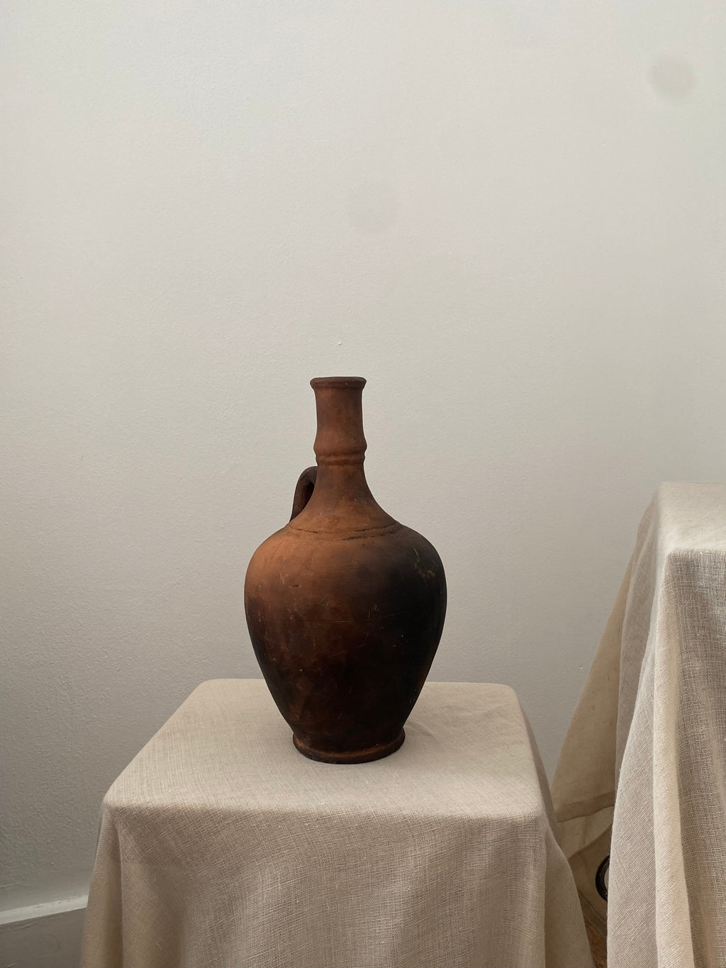 Brown antique clay pitcher on a white pedestal against a plain background