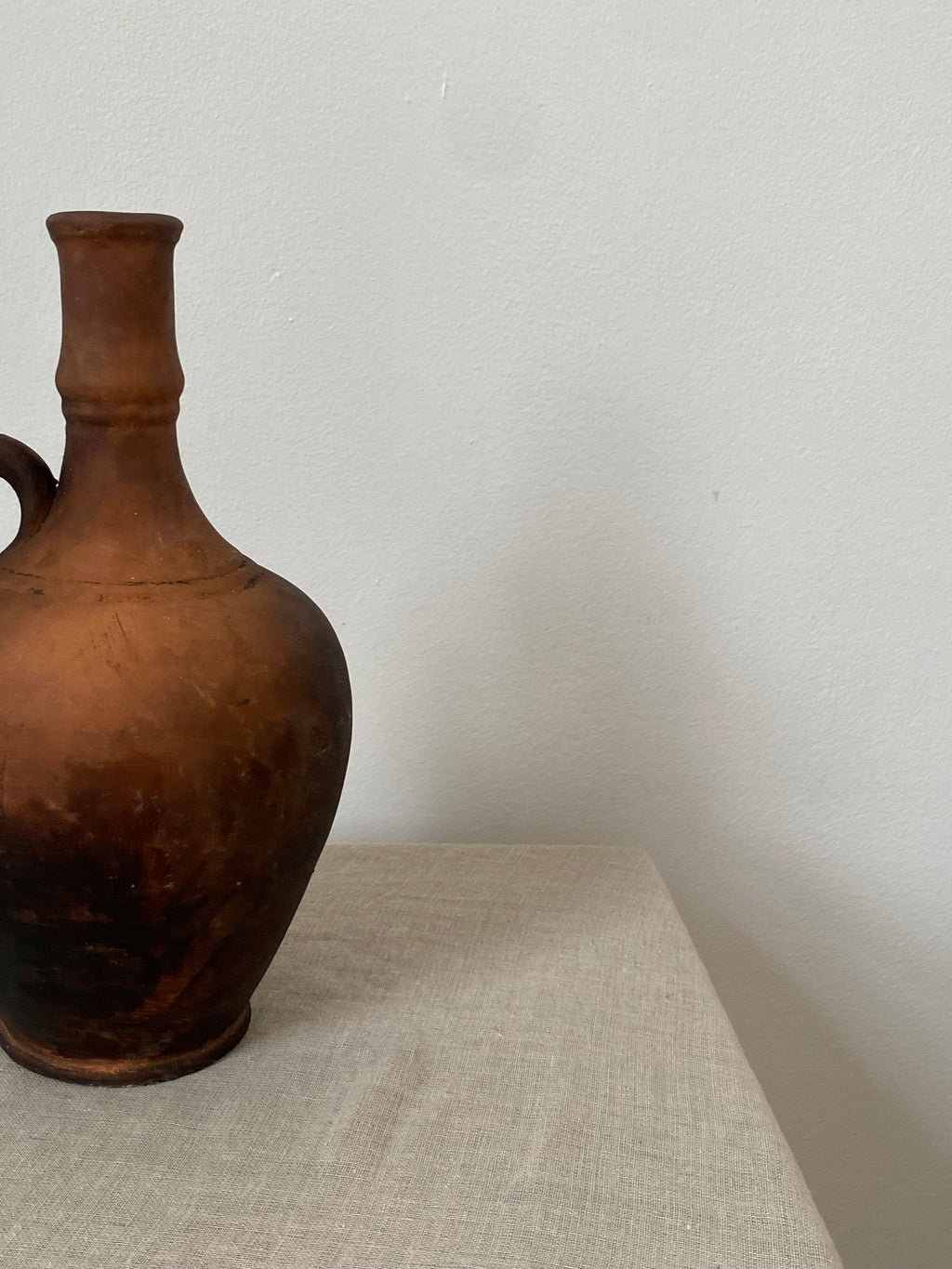 Brown antique terracotta clay pitcher on a linen cloth with a neutral background