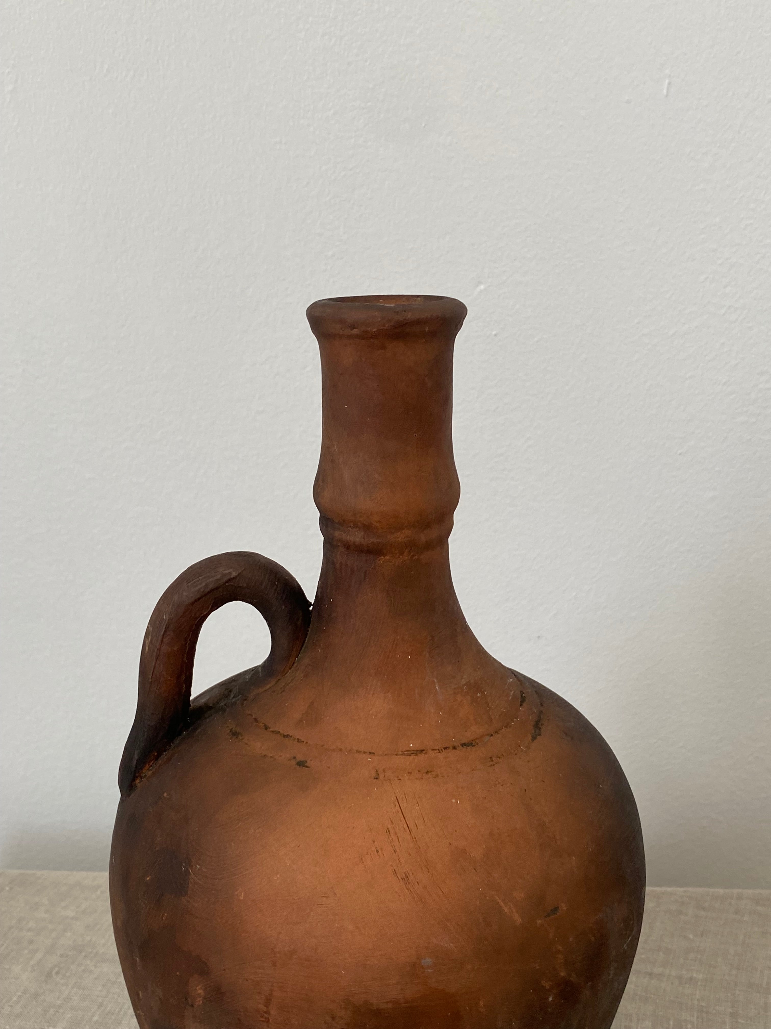 Brown terracotta clay pitcher with a handle on a light gray background