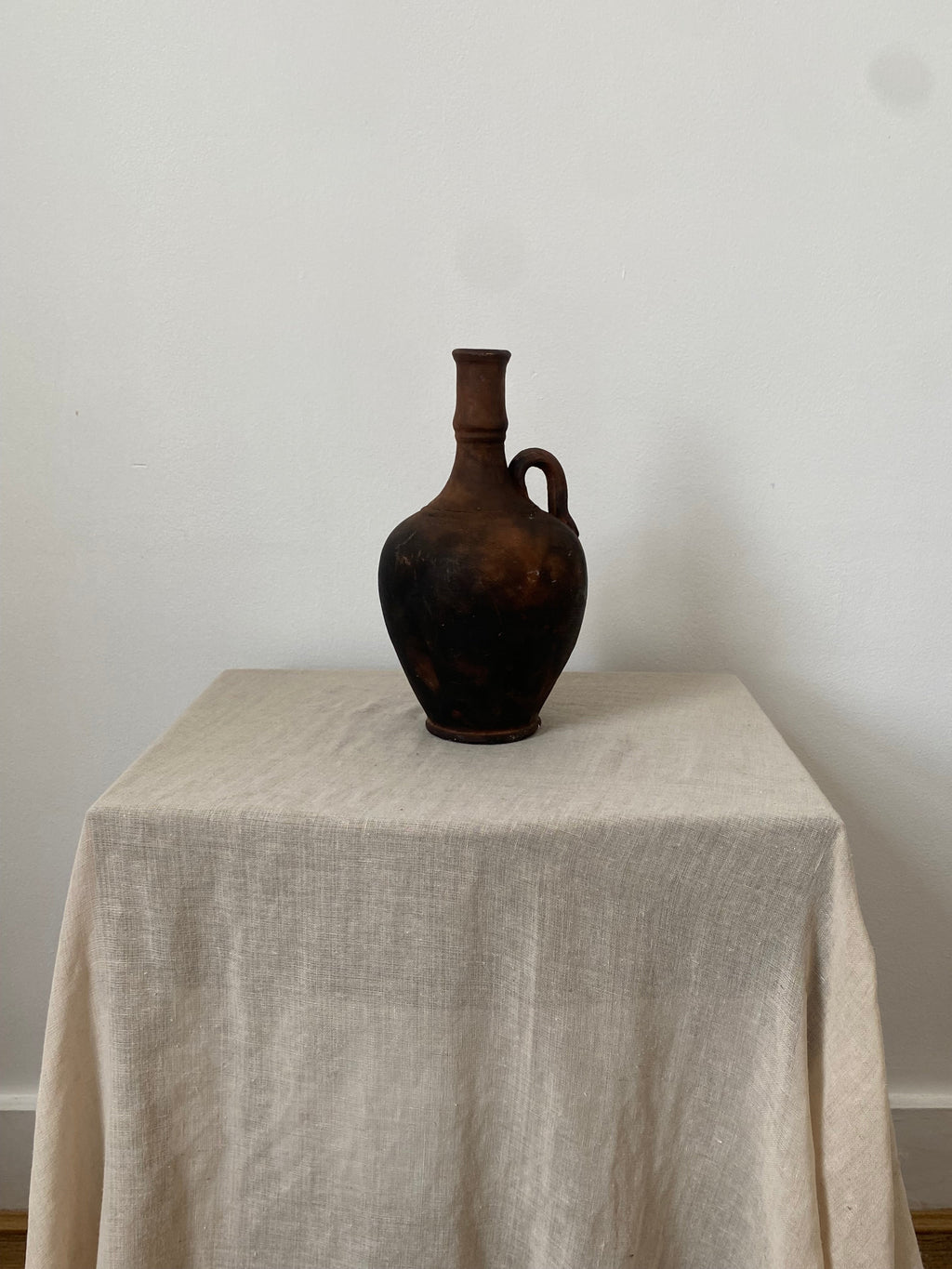 Brown antique terracotta pitcher on a beige linen cloth with a white background